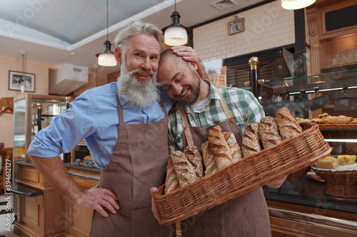 Happy proud senior male baker hugging his son, working together at bakery store