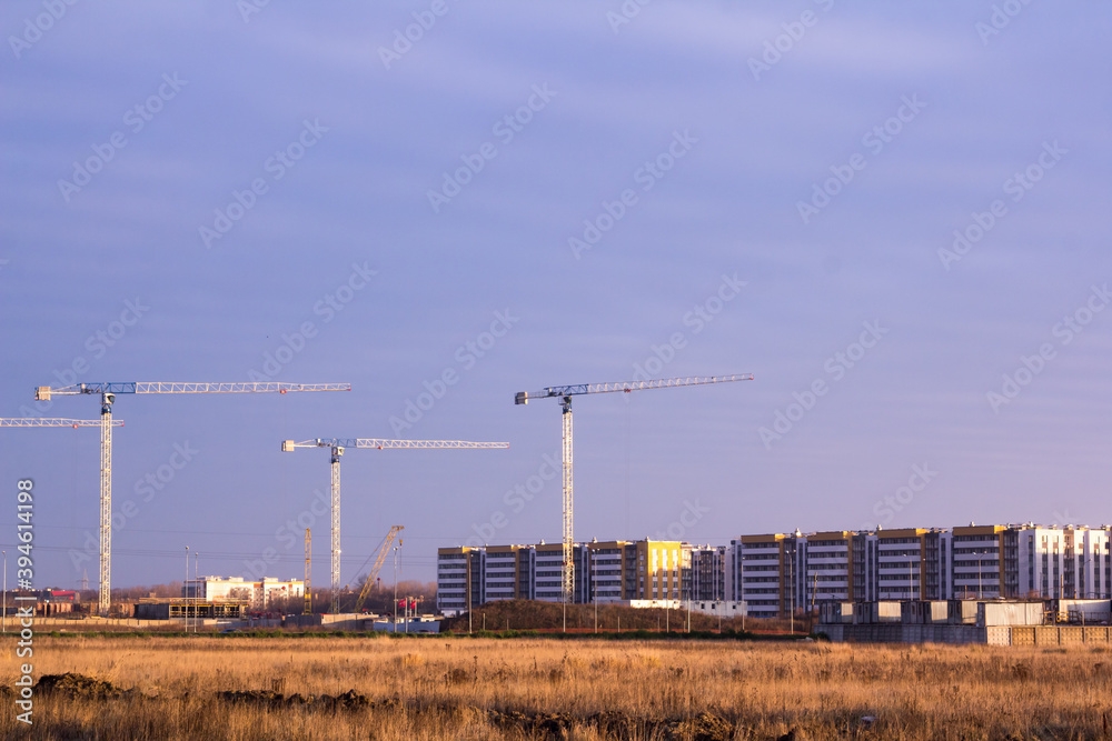 construction site with tower cranes in a field against a dark blue sky construction site with tower cranes in a field against a dark blue sky