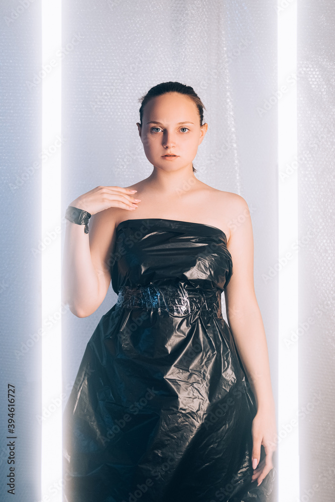 Futuristic fashion. Plastic pollution. Zero waste. Save nature. Sensual  woman posing in black creative design cellophane garbage bag dress on light  illuminated bubble wrap background. Stock Photo | Adobe Stock