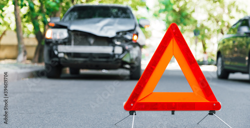 Red emergency stop triangle sign on road during a car accident. Broken gray car during road traffic accident. Car crash traffic accident on city road after collision. Long web banner