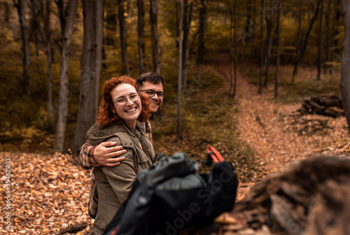 Portrait of two young hikers with backpack sitting on collapsed trunk resting after walking in forest.