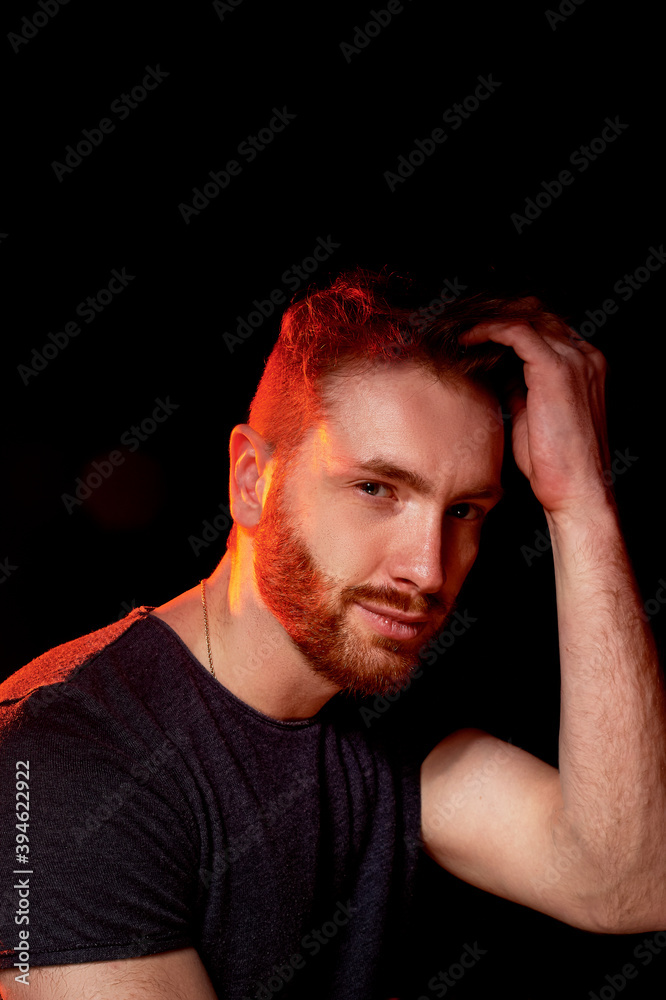 A brutal man on a dark background in the light of a red lamp.