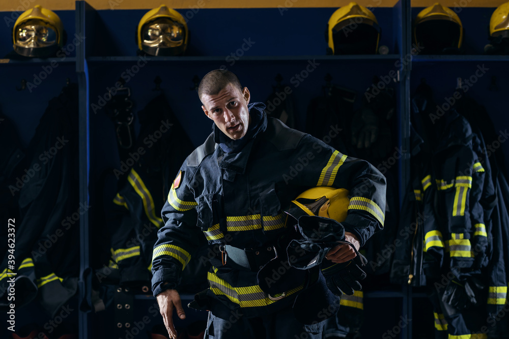Obraz premium Brave young attractive firefighter in protective uniform holding helmet under armpit after action while standing in fire station.