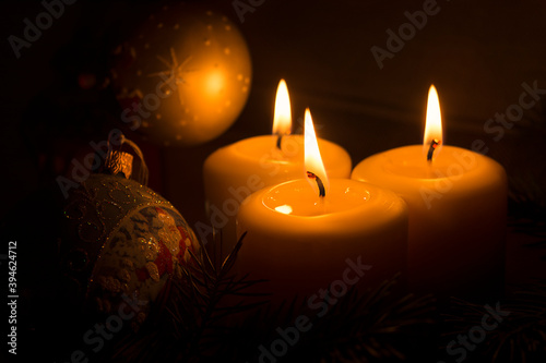 White candles with Christmas tree branches and Christmas tree toys on a dark background. The candle flame gives a sense of celebration and waiting for a gift. Holiday fairy-tale greeting card