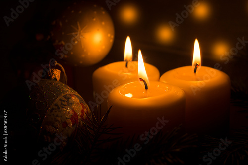 White candles with Christmas tree branches and Christmas tree toys on a dark background. The candle flame gives a sense of celebration and waiting for a gift. Holiday fairy-tale greeting card