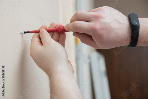 Worker manually tightening an artwork hang screw into a drilled hole in white wall with screwdriver  renovating  decorating and improving home
