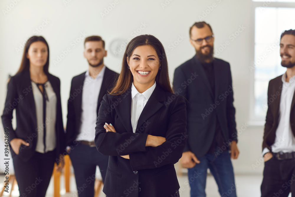 Happy smiling female company leader with team of employees standing in background Happy smiling female company leader with team of employees standing in background