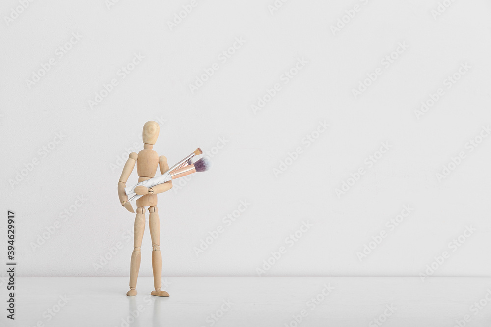 Wooden mannequin with makeup brushes on light background Wooden mannequin with makeup brushes on light background