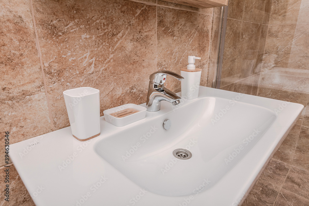 Fototapeta premium Close up of a snow-white sink in a cozy tiled bathroom in light colors. White bathroom accessories