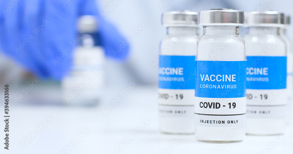Corona virus Vaccine concept. Female doctor hands in blue medical gloves with transparent liquid coronavirus vaccine bottle and syringe for injection in the laboratory. Research and development of new