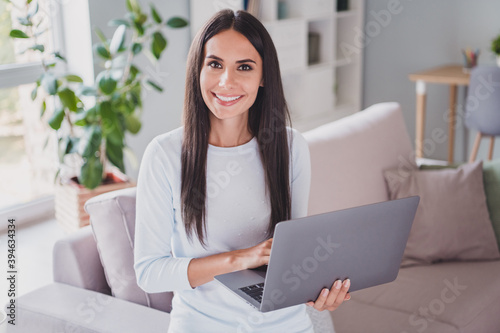 Photo of charming brown haired woman wear white sweater hold computer good mood indoor in house living room