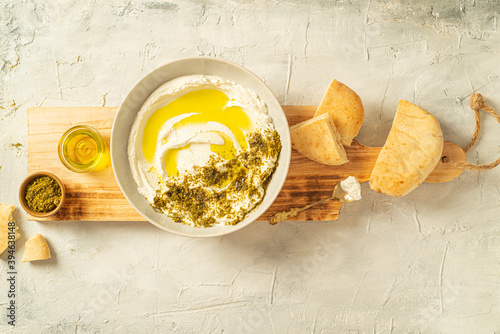 Popular middle eastern appetizer labneh or labaneh, soft white goat milk cheese with olive oil, hyssop or zaatar, served with pita bread on a wooden plate on a grey table, 