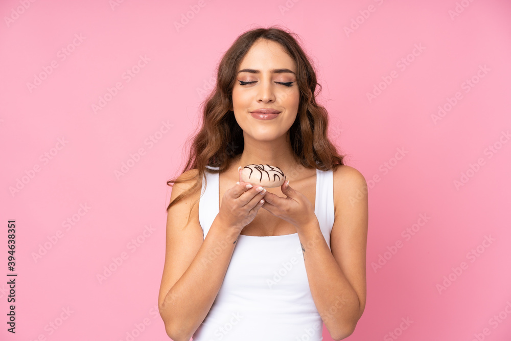 Young woman over isolated pink background holding a donut Young woman over isolated pink background holding a donut