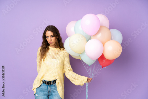Young woman catching many balloons over isolated on purple background pleading