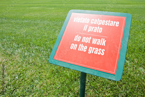 Do not walk on the grass - concept image white text on signboard and fresh green lawn - text in English and Italian photo