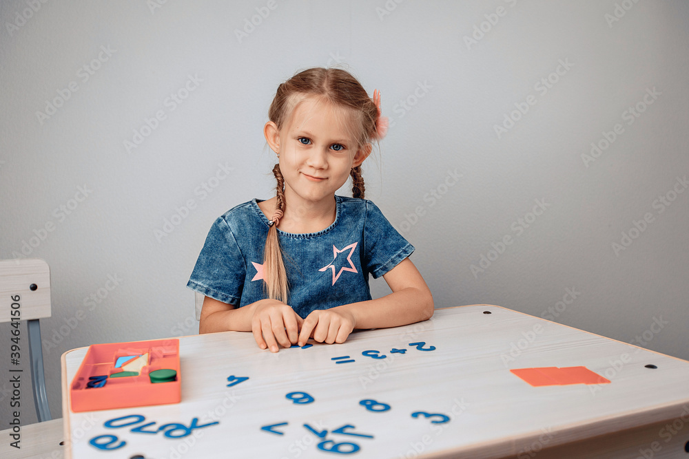 Portrait of a pretty smiling lovelylittle child sitting at a white table and studying numbers. Knowledges concept. photo with noise Portrait of a pretty smiling lovelylittle child sitting at a white table and studying numbers. Knowledges concept. photo with noise