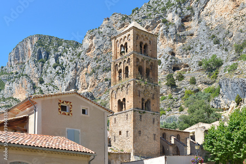 Moustiers-Sainte-Marie at the foot of the mountain and church of Notre-Dame-de-l'Assomption with its square bell tower . Moustiers-Sainte-Marie is a commune in the Alpes-de-Haute-Provence department