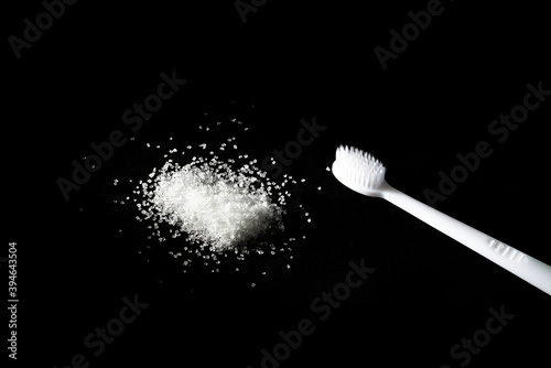 new white toothbrush and a handful of sprinkled sugar on a dark background. dental treatment and caries concept