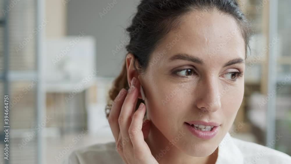Close up of young Caucasian woman with curly hair answering telephone call through wireless earphones Close up of young Caucasian woman with curly hair answering telephone call through wireless earphones