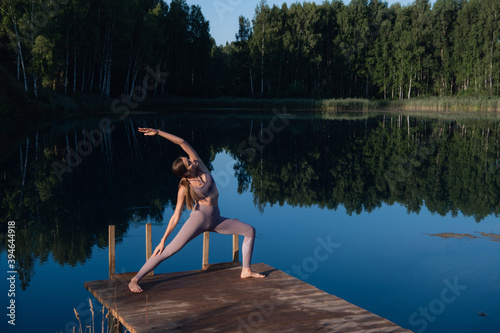 Woman doing yoga on a forest lake. Beautiful girl doing exercises on stretching and flexibility outdoors