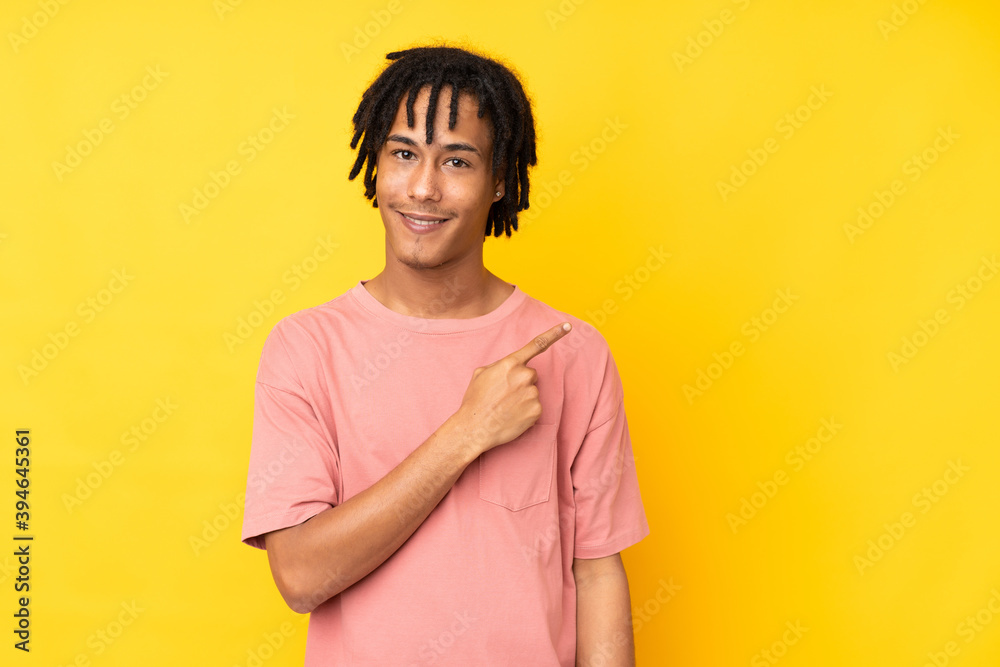 Young african american man isolated on yellow background pointing to the side to present a product
