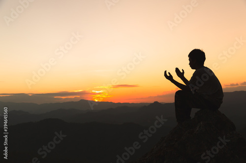 Silhouette of young man hands open palm up worship and praying to god at sunrise, Christian Religion concept background.
