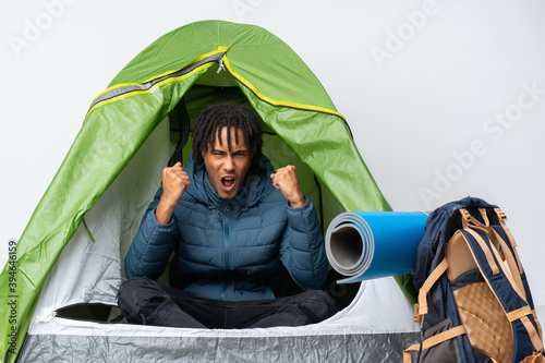 Young african american man inside a camping green tent frustrated by a bad situation