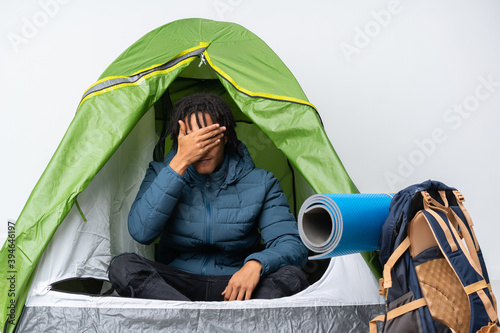 Young african american man inside a camping green tent covering eyes by hands. Do not want to see something