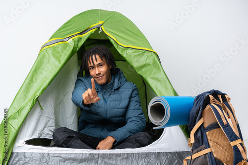 Young african american man inside a camping green tent showing and lifting a finger