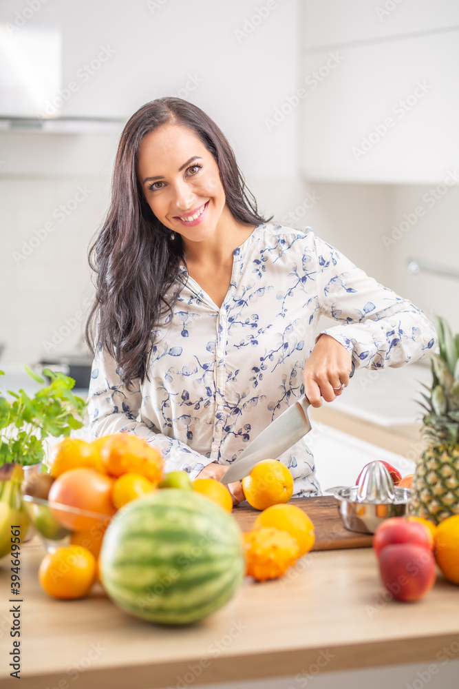 Smiling young woman slicing orange fruit in the kitchen.