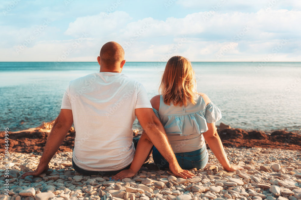 An adult couple, a plus-size man and woman, sit on the beach, admiring the ocean. Rear view. The concept of Valentine's day An adult couple, a plus-size man and woman, sit on the beach, admiring the ocean. Rear view. The concept of Valentine's day