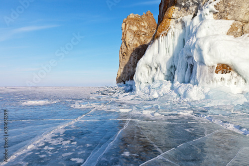 Beautiful landscape of frozen lake Baikal on a Sunny day in February. Blue ice with cracks and hummocks near the icy rocks of Olkhon island. Winter holidays, ice travel. Natural background