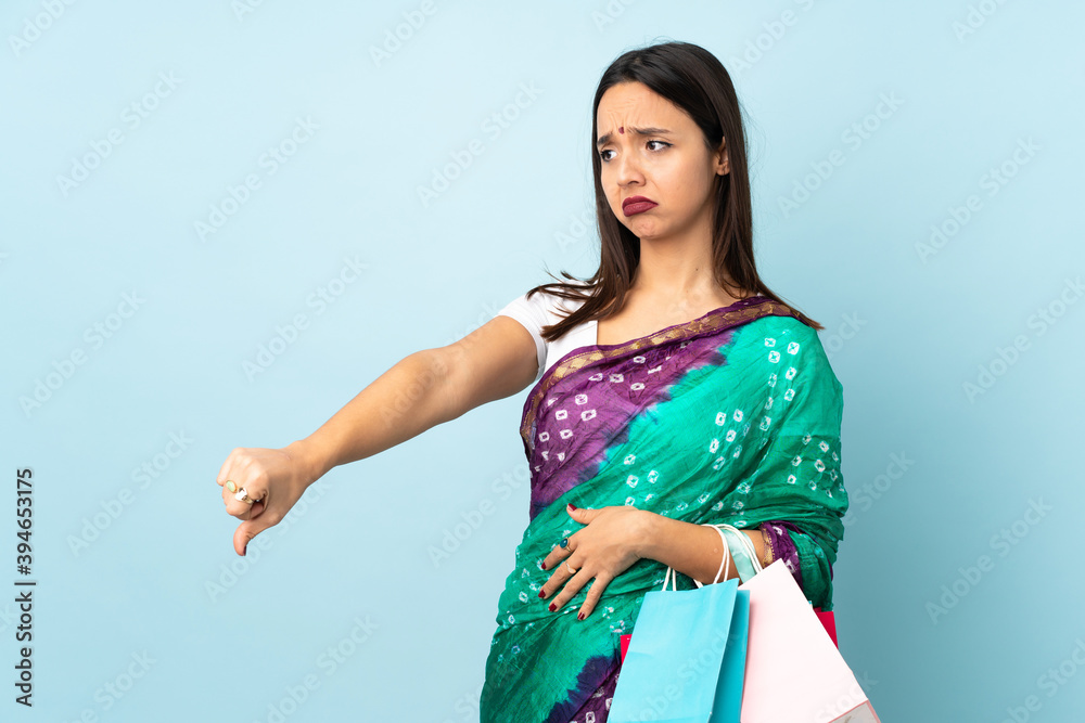 Young Indian woman with shopping bags showing thumb down with negative expression Young Indian woman with shopping bags showing thumb down with negative expression