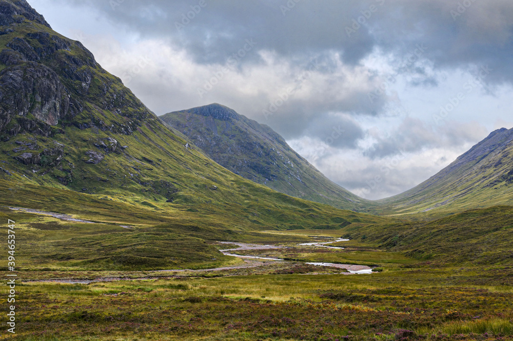 Glencoe valley in the Highlands of Scotland. The Glencoe river meanders between rocky mountain slopes across moorland covered with wild flowers and purple heather. Glencoe valley in the Highlands of Scotland. The Glencoe river meanders between rocky mountain slopes across moorland covered with wild flowers and purple heather.