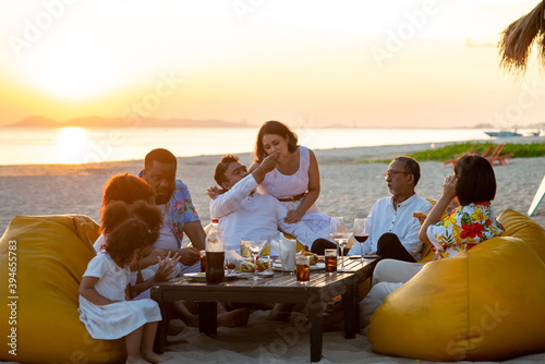 Group of multiethnic family friends enjoy dinner party together on the beach at sunset. Diverse family with child girl, adult and senior couple relax and having fun together on summer holiday vacation © CandyRetriever 