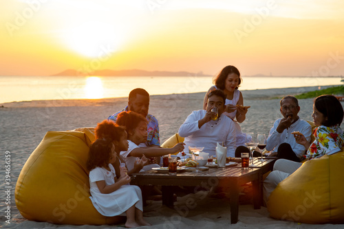 Group of multiethnic family friends enjoy dinner party together on the beach at sunset. Diverse family with child girl, adult and senior couple relax and having fun together on summer holiday vacation © CandyRetriever 