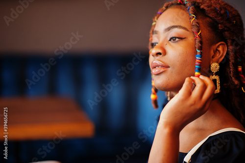Face portrait of lovely african american woman with dreadlocks at cafe. Beautiful cool fashionable black young girl indoor.