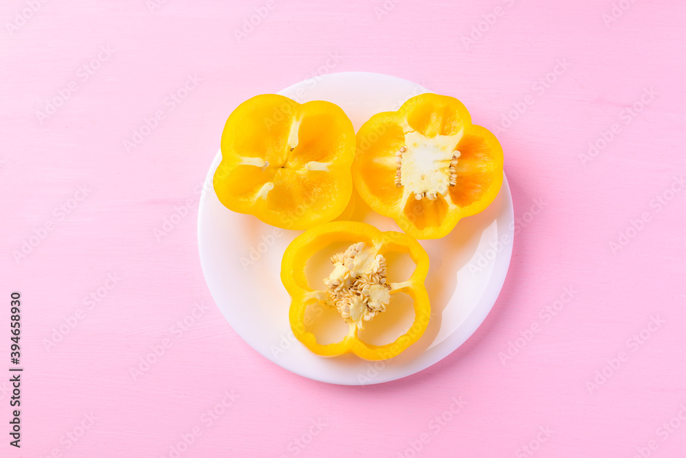 Sliced yellow bell peppers on white plate with pink background, Top view