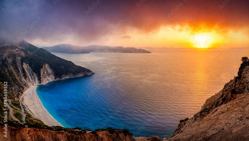 Elevated, panoramic view to the famous Myrtos beach on the island of Kefalonia, Greece, with blue and turquoise sea during sunset time with very low clouds