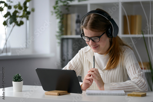 A young, purposeful girl with a tablet in a bright modern office, a student at distant learning at home, online communication with friends