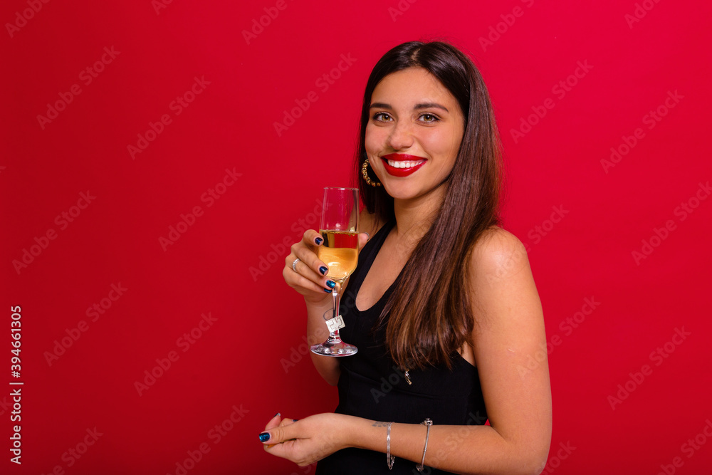 Happy pretty lady dressed black shirt with red lips is posing at camera with a glass of champagne over red background Happy pretty lady dressed black shirt with red lips is posing at camera with a glass of champagne over red background