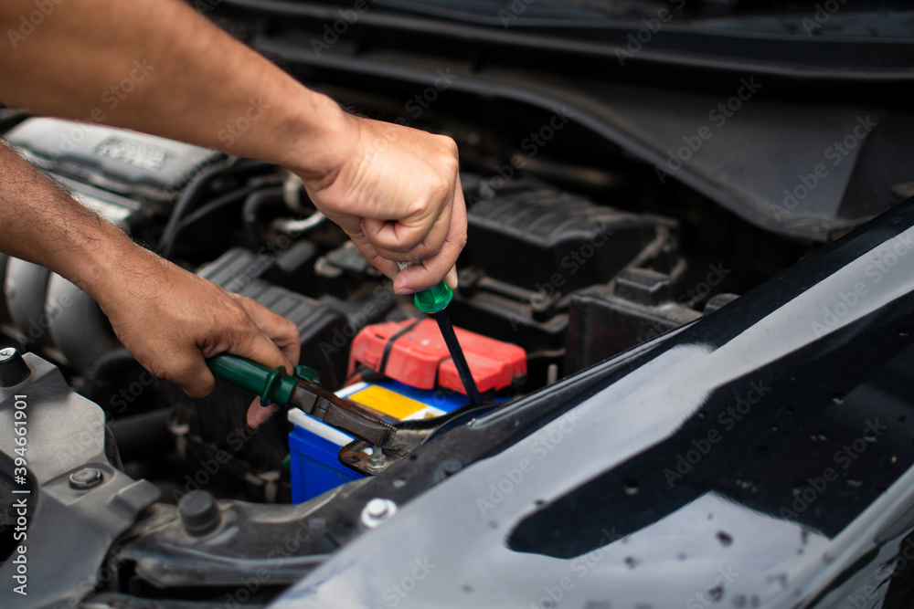 Closeup, The hands of a male technician are using a tool to replace the car battery, parked at home. Black car, the battery is damaged. Tools have pliers and screwdrivers. Closeup, The hands of a male technician are using a tool to replace the car battery, parked at home. Black car, the battery is damaged. Tools have pliers and screwdrivers.
