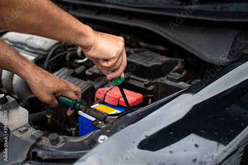 Closeup, The hands of a male technician are using a tool to replace the car battery, parked at home. Black car, the battery is damaged. Tools have pliers and screwdrivers. © Mdisk