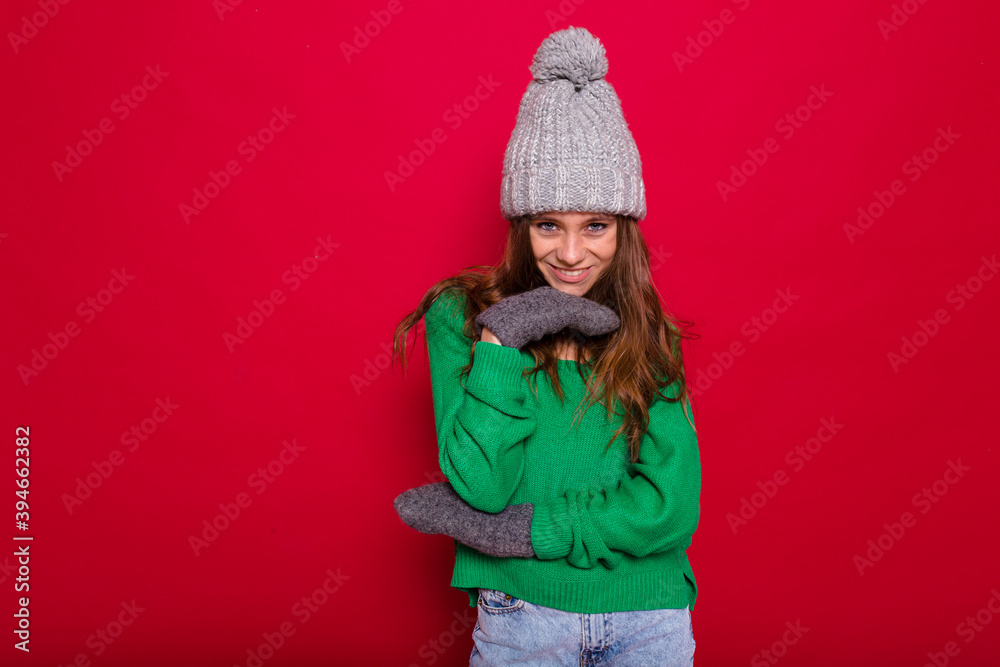 Enchanting girl wears knitted sweater and cap isolated on red background . Indoor photo of happy long-haired woman having fun in studio Enchanting girl wears knitted sweater and cap isolated on red background . Indoor photo of happy long-haired woman having fun in studio