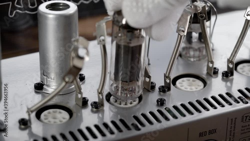 An electronic engineer installs a new radio tube in the power amplifier. Vintage amps are popular. photo