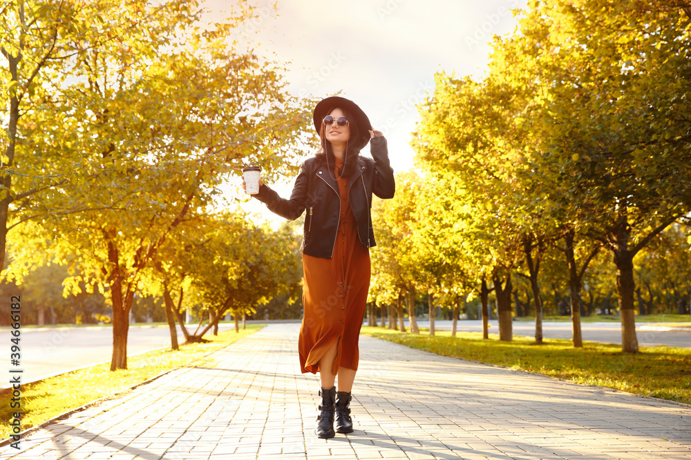 Fototapeta premium Beautiful young woman with cup of coffee wearing stylish clothes in autumn park