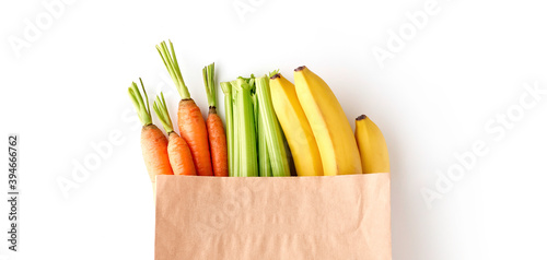 Fototapeta Naklejka Na Ścianę i Meble -  Paper grocery bag full of healthy fruits and vegetables - banana, carrots and celery, top view isolated on white background