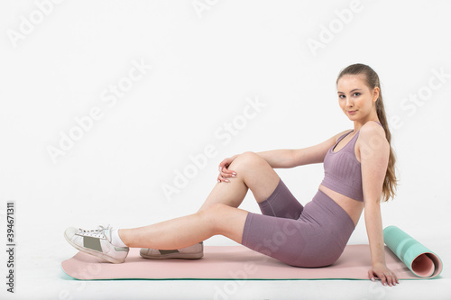 Young sporty woman in sportswear sitting and resting on fitness mat.