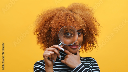 Funny young african american black woman with magnifier in hand shows eye through magnifying glass. High quality photo