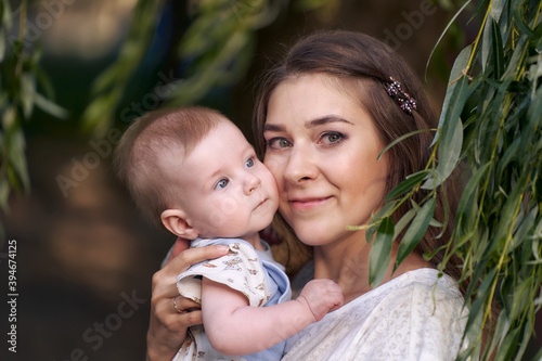 Portrait of a young mother with a baby in her arms by a weeping willow. Close-up. mom's hug.